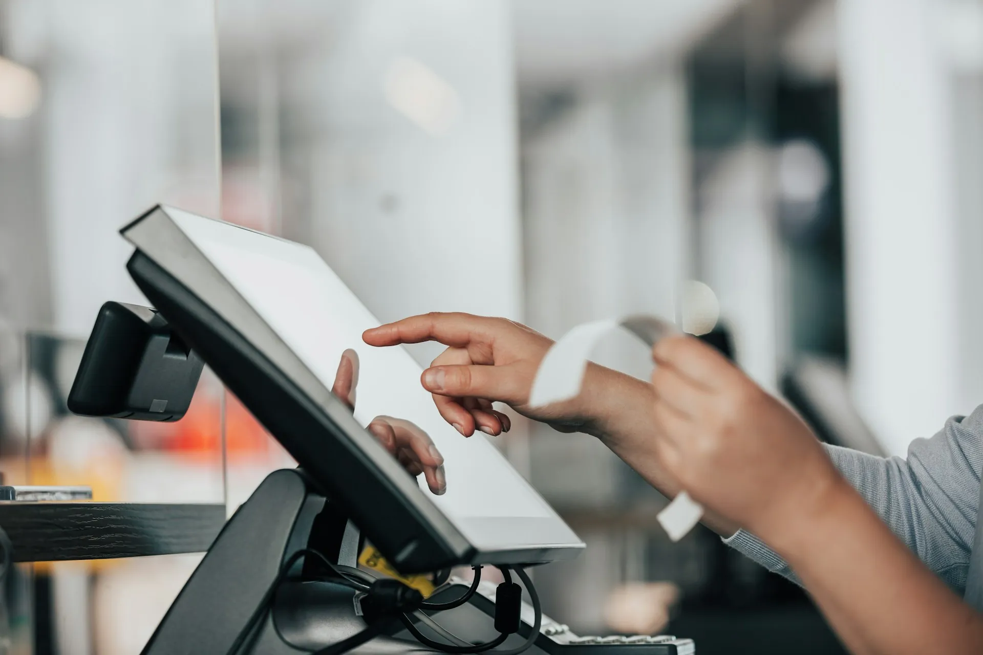 Hands operating a touchscreen POS terminal at a retail counter while a receipt prints