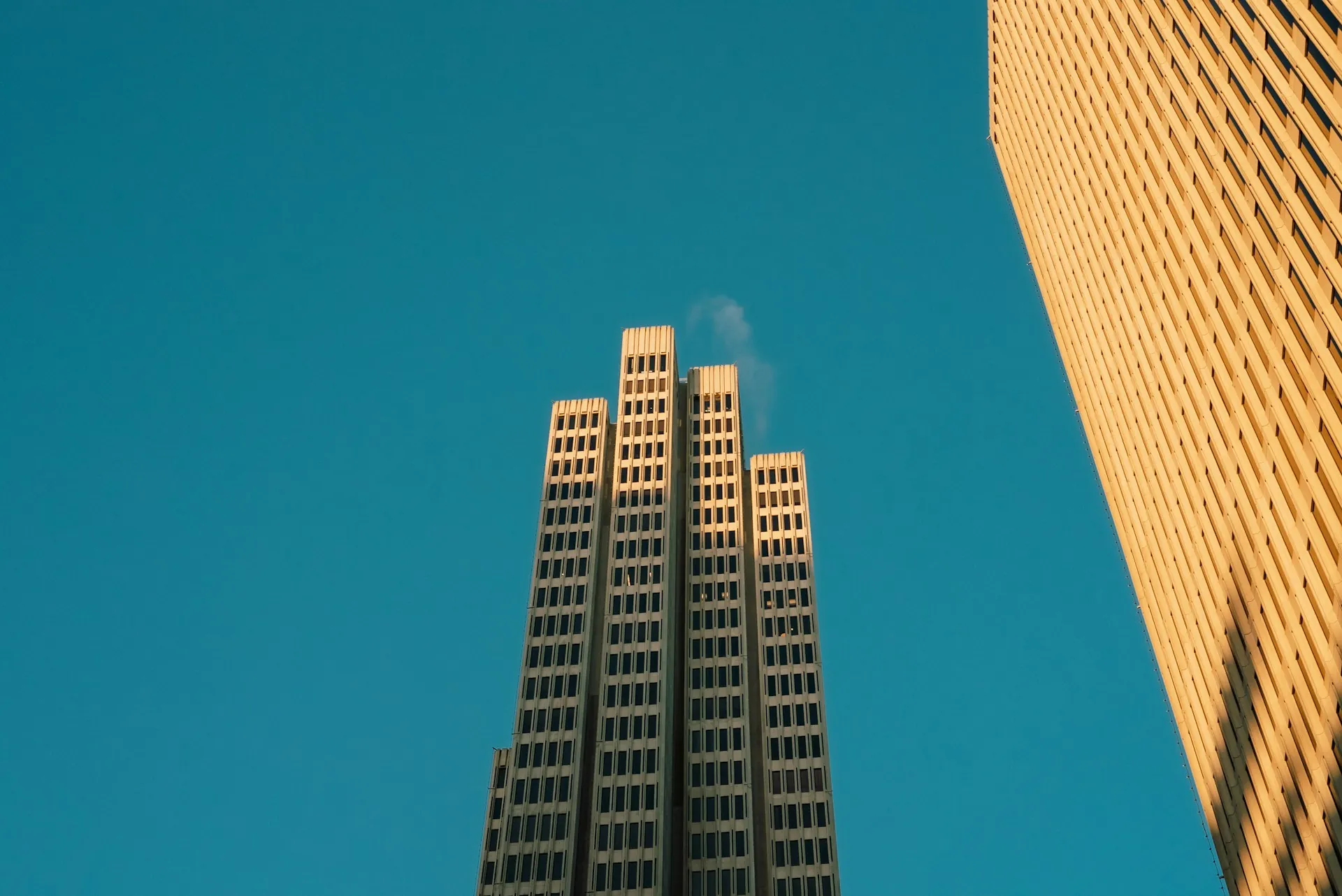Twin tower buildings rising against a clear blue sky in golden hour light, viewed from below