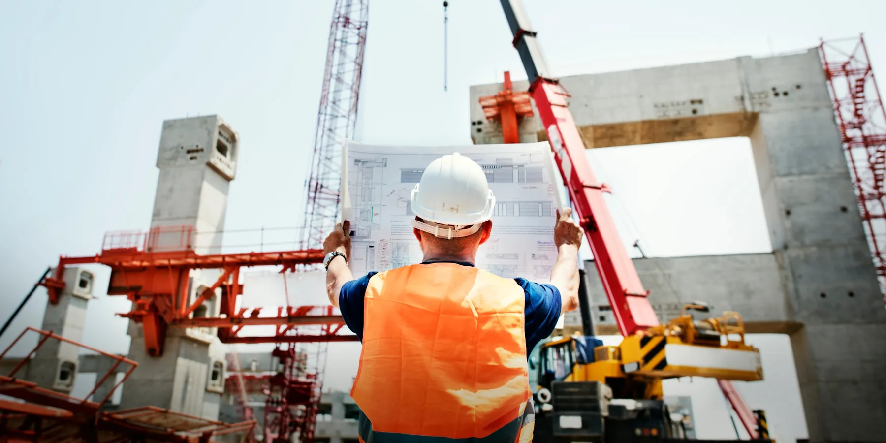 A site manager holding up plans against a part-built structure, checking the detail